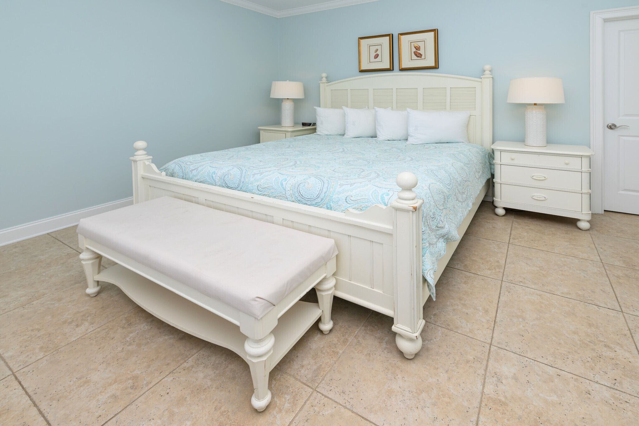 A bedroom with a bed, nightstands, a bench, and two framed pictures on the wall.
