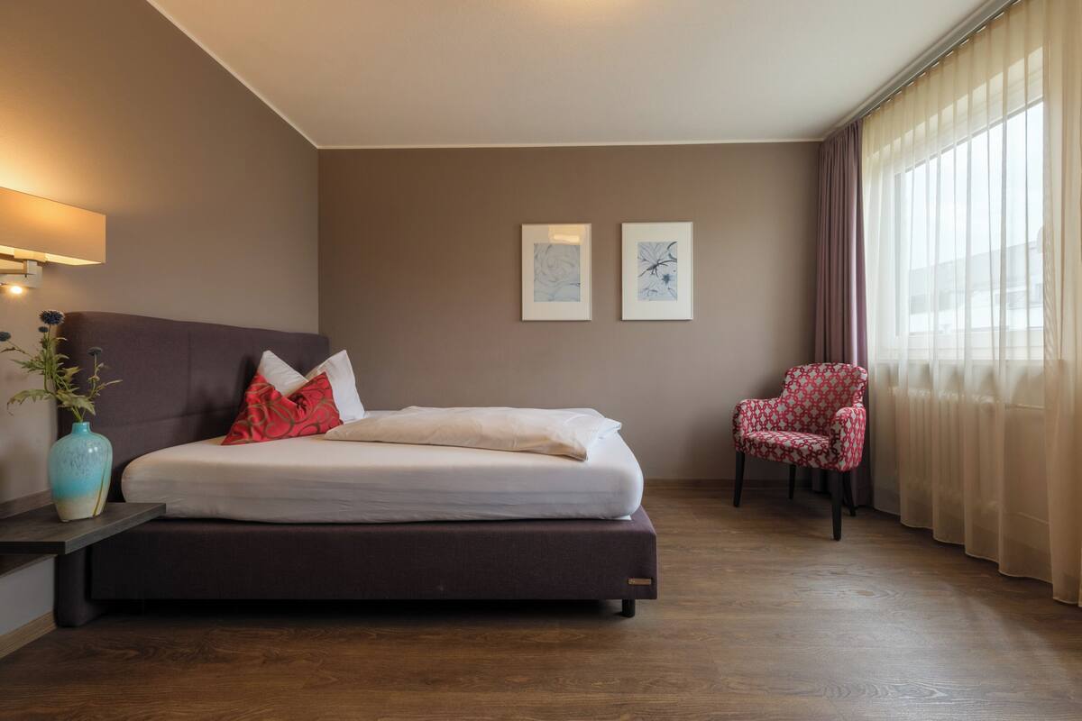 Habitació d'hotel amb un llit, una cadira, un ram de flors i dos quadres a la paret.