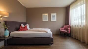 Una habitación de hotel con una cama, una silla, un florero con flores y dos cuadros en la pared.