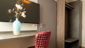 A modern room with a flat-screen TV, a vase with dried flowers, a patterned chair, and a wooden floor. - Hotel Staffler & Schreiners Restaurant (Odelzhausen)