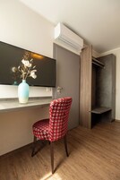 Una habitación moderna con televisión de pantalla plana, un jarrón con flores secas, una silla estampada y suelo de madera.