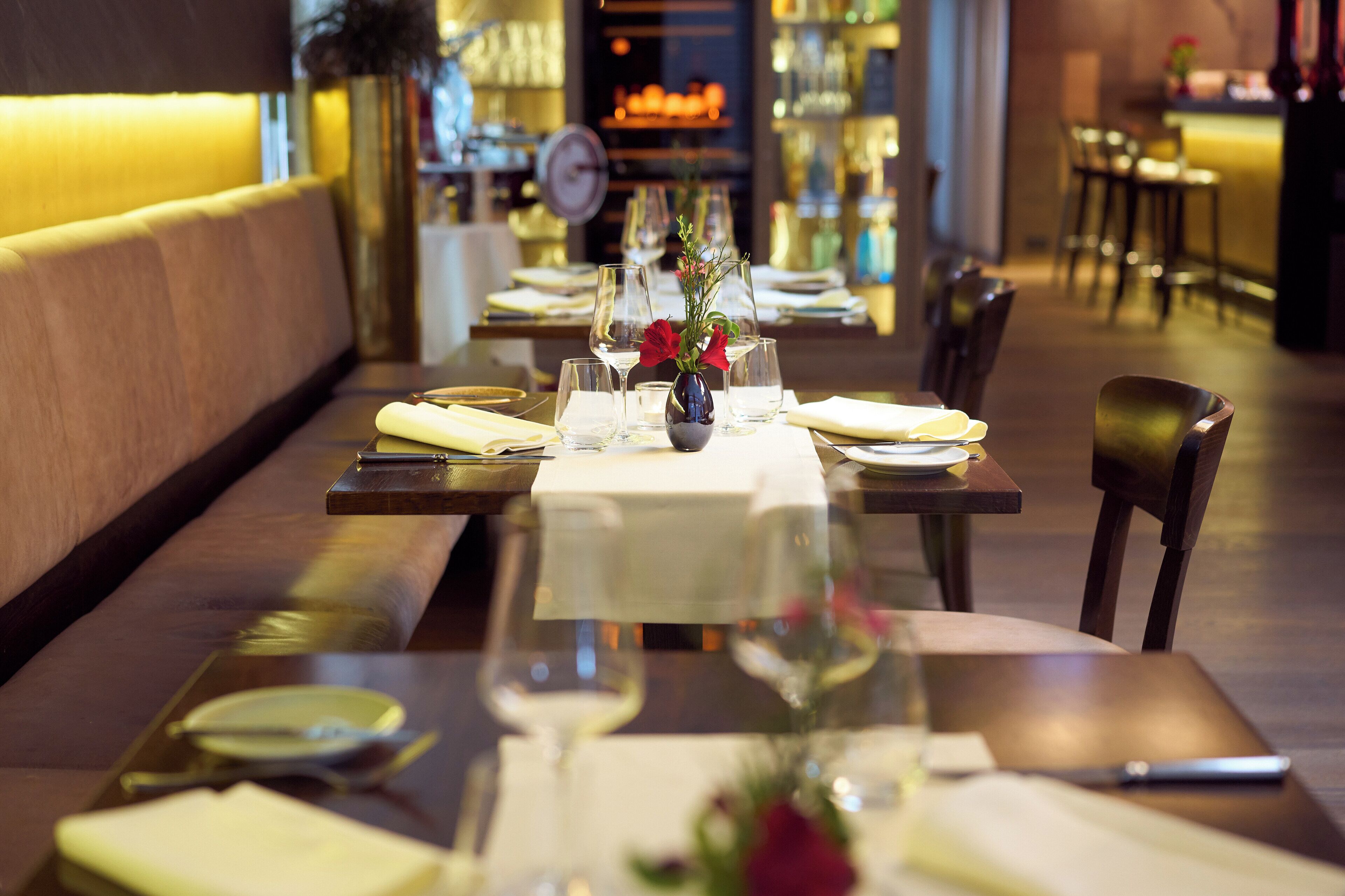 A restaurant with tables set for dining, featuring a vase with flowers and wine glasses.