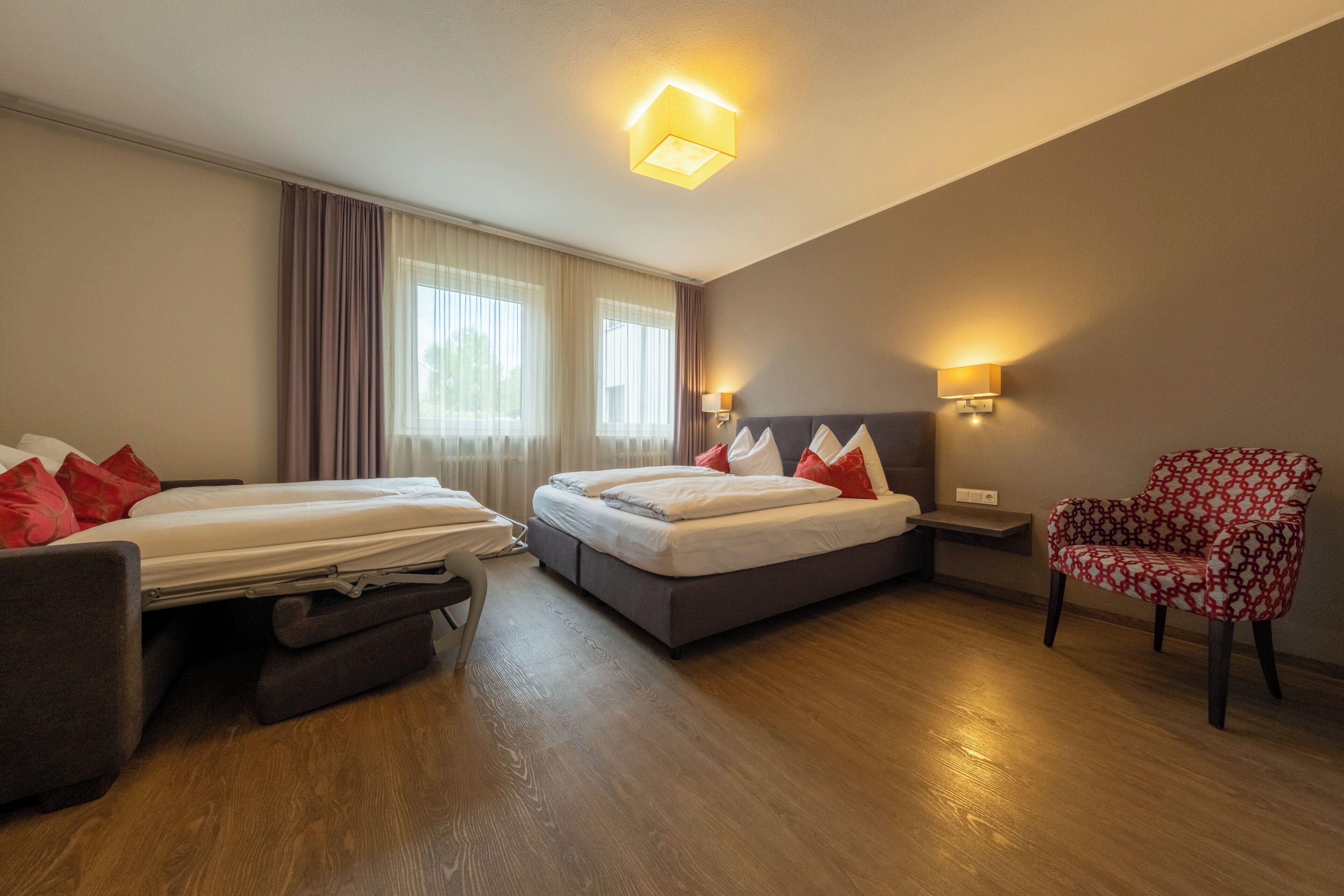 A hotel room with two beds, a chair, and a nightstand with lamps.