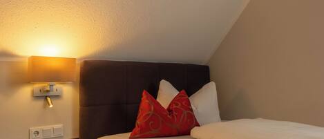A hotel room with a bed, a nightstand, a wall-mounted lamp, and a wooden floor.