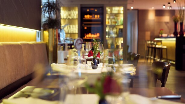 A restaurant with a bar area, tables set with glasses and cutlery, and a vase with flowers on the table. - Hotel Staffler & Schreiners Restaurant (Odelzhausen)