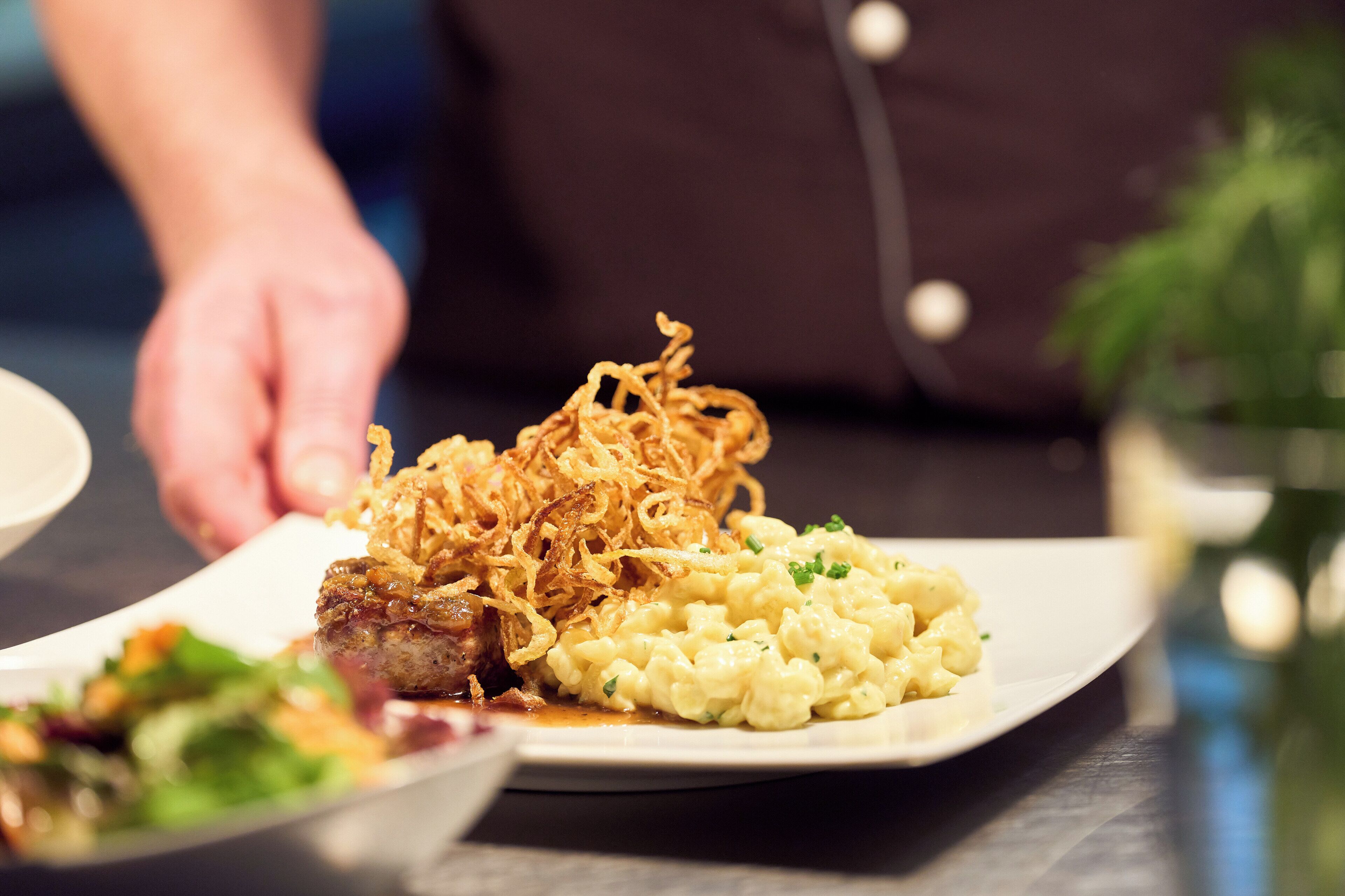 A plate of food with a steak topped with fried onions, macaroni salad, and a side salad.