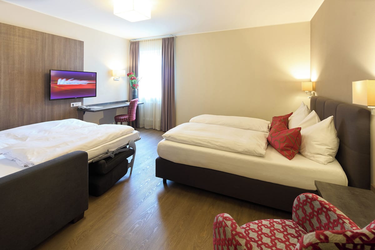 Habitació d'hotel amb dos llits, una taula de treball, televisió i finestra amb cortines.