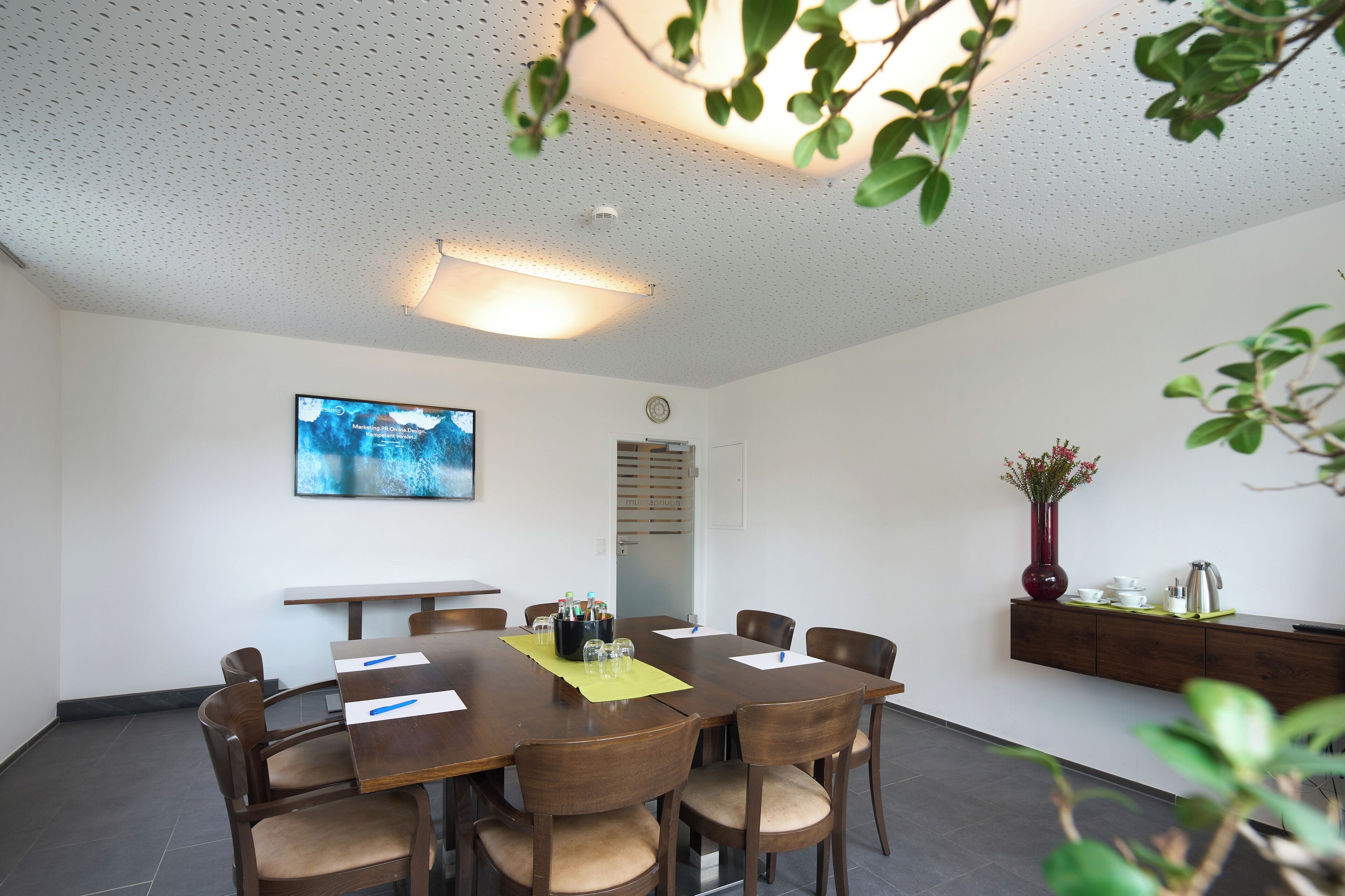 A conference room with a large table, chairs, a clock, and a wall-mounted TV.