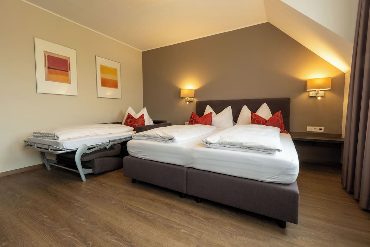 Habitació d'hotel amb dos llits, un sofà-llit i dues làmpades fixades a la paret.
