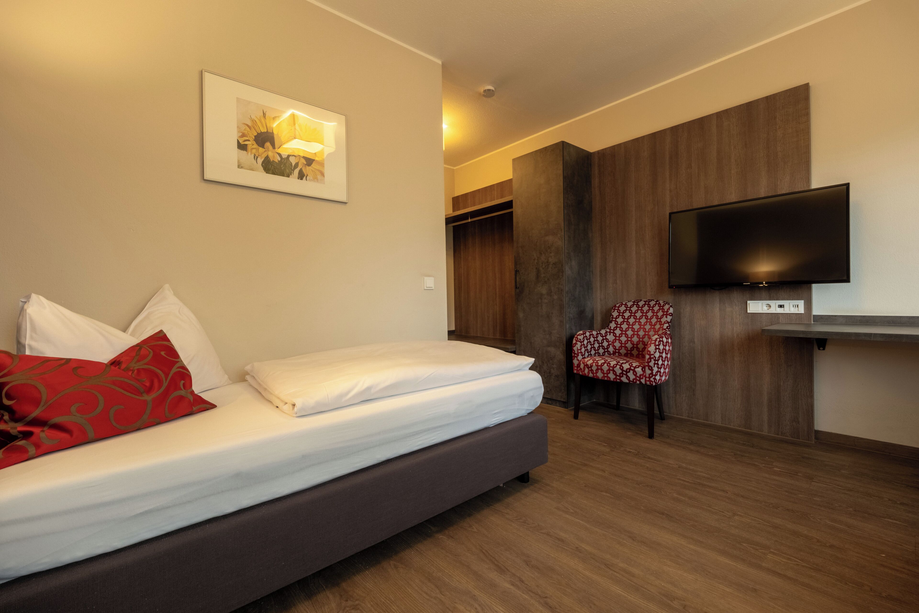 A hotel room with a bed, a TV, a chair, and a wooden wardrobe.