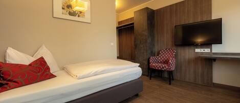 A hotel room with a bed, a TV, a chair, and a wooden wardrobe.