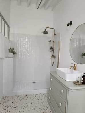 A bathroom with a shower, a sink with a gold faucet, a mirror, and a terrazzo floor.