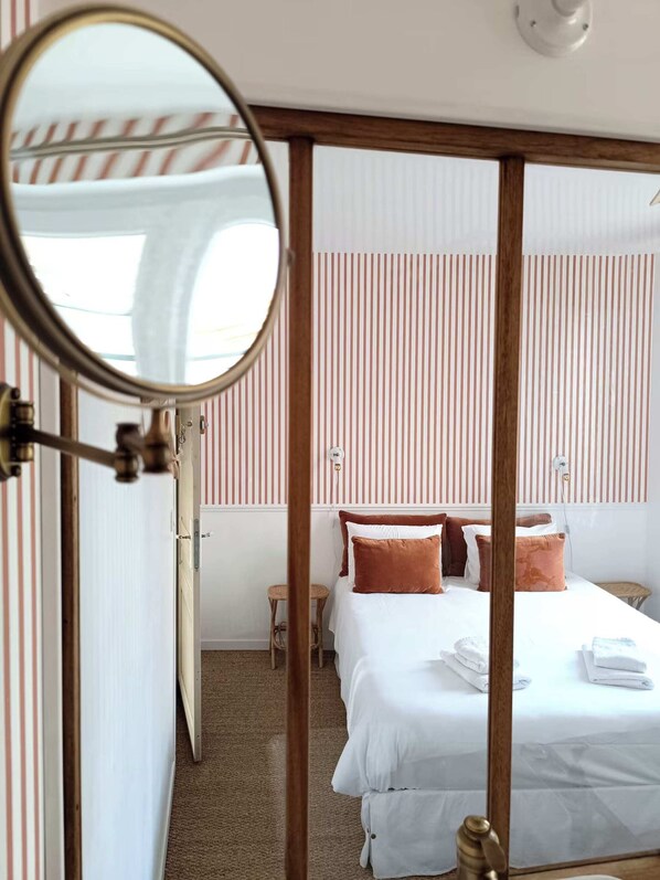 Una habitación de hotel con una cama, un taburete pequeño y un espejo.