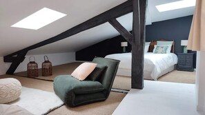 A bedroom with a sloped ceiling, a green armchair, a bed with white bedding, and two lanterns on the floor.