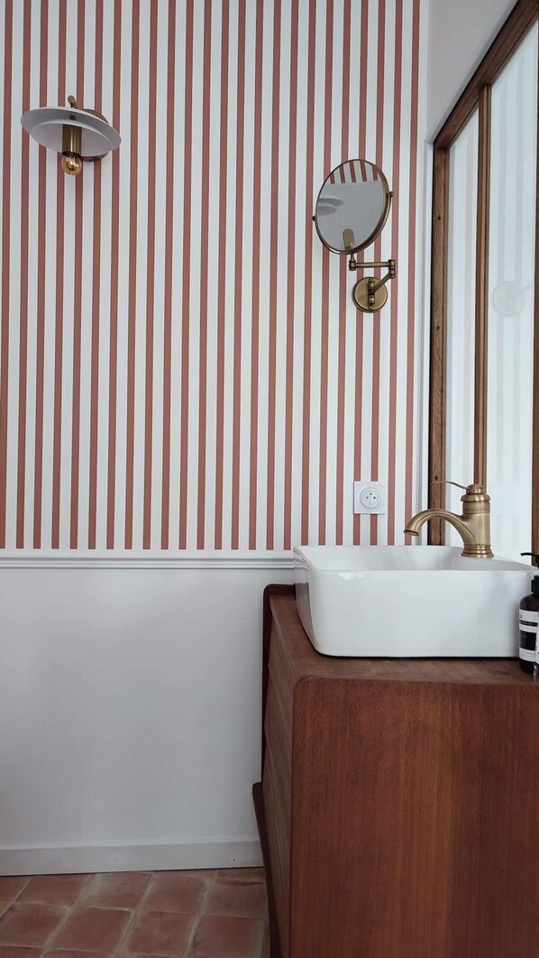 A bathroom with a white bathtub, a wooden vanity, a round mirror, and a wall with vertical stripes.