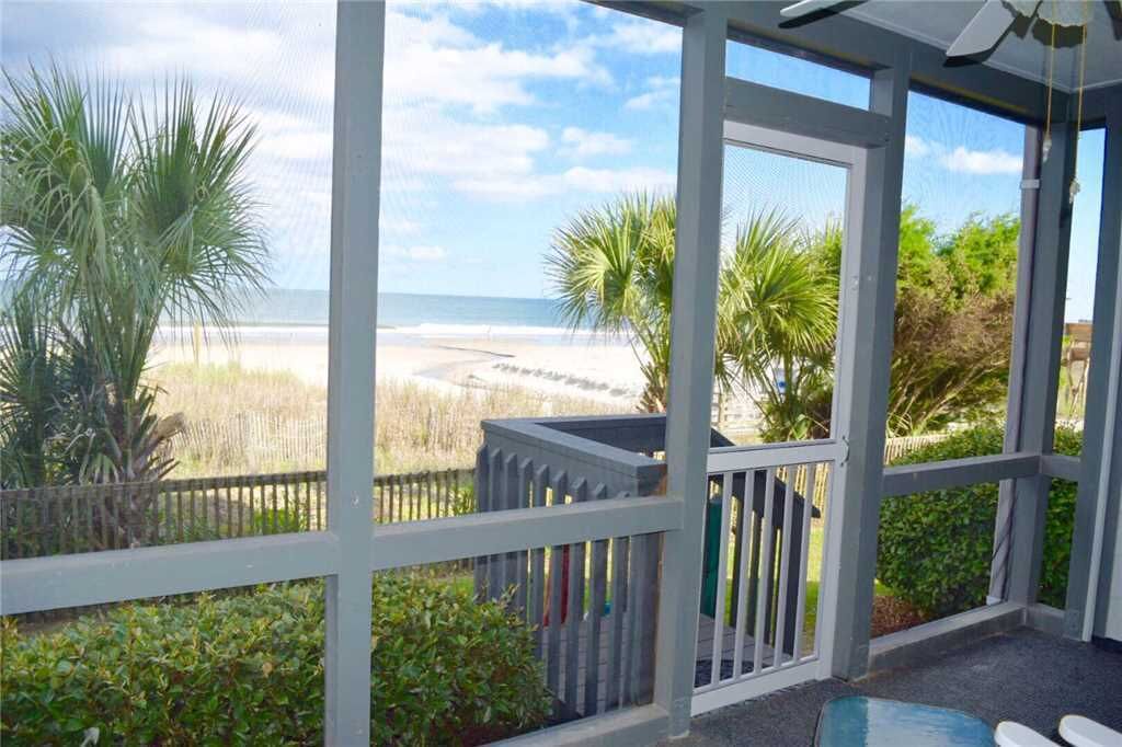 A covered outdoor area with a view of the beach, a wooden fence, and some greenery.