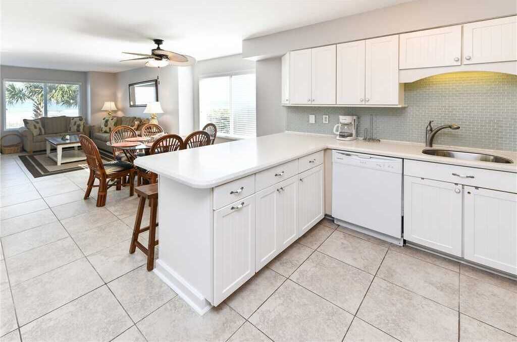 Una cocina moderna con muebles blancos, una isla central y un comedor con sillas de madera.