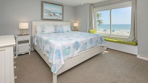 Un dormitorio con cama, mesitas de noche, ventana con vista a la playa y ventilador de techo.