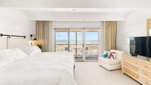 A hotel room with a large bed, a TV, a small sofa, and a balcony with a view of the beach. - Beach Place 14 2 Bedroom Townhouse (Ocean City)
