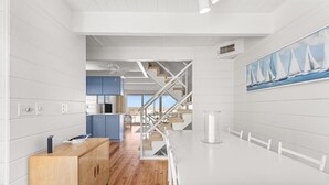 A modern kitchen with wooden cabinets, a white dining table, and a staircase leading to a balcony. - Beach Place 14 2 Bedroom Townhouse (Ocean City)