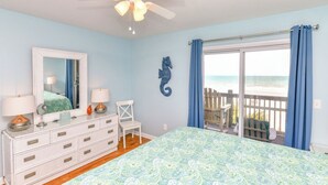 Un dormitorio con cama, cómoda y un amplio ventanal con vista a la playa.