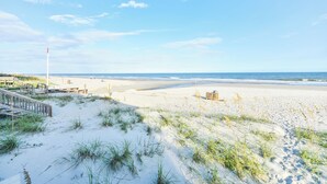 A beach with a wooden boardwalk leading to the shore, sandy dunes with sparse vegetation, and a clear blue sky. - Oceanfront 3 BR Condo with a Shared Pool! Sea Cloisters II 101B (Surfside Beach)