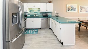 A modern kitchen with stainless steel appliances, white cabinets, a glass countertop, and a backsplash with teal tiles. - Oceanfront 3 BR Condo with a Shared Pool! Sea Cloisters II 101B (Surfside Beach)