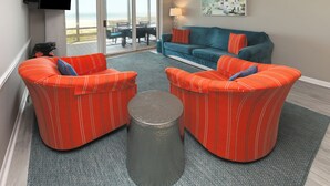 A living room with a sofa set, a coffee table, and a TV mounted on the wall. - Oceanfront 3 BR Condo with a Shared Pool! Sea Cloisters II 101B (Surfside Beach)
