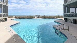 A swimming pool with a view of the ocean, surrounded by a wooden deck and a covered area. - Oceanfront 3 BR Condo with a Shared Pool! Sea Cloisters II 101B (Surfside Beach)