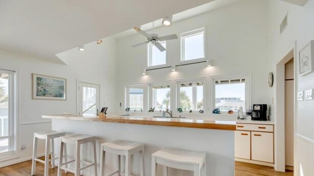 A modern kitchen with a central island, bar stools, and a ceiling fan.