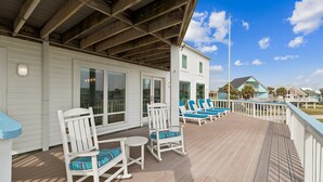 A wooden deck with white railings, blue cushioned chairs, and a clear view of the surrounding houses.