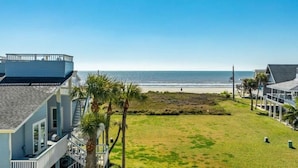 A coastal property with a grassy lawn, a beach view, and a two-story building with a balcony.