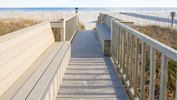 A wooden boardwalk leading to a beach with a lamp post and benches.
