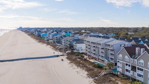 A beachfront hotel with multiple-story buildings, a beach in the foreground, and a pier extending into the water.