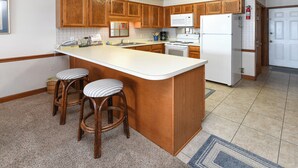 A kitchen with wooden cabinets, a white refrigerator, a microwave, a stove, and two bar stools.