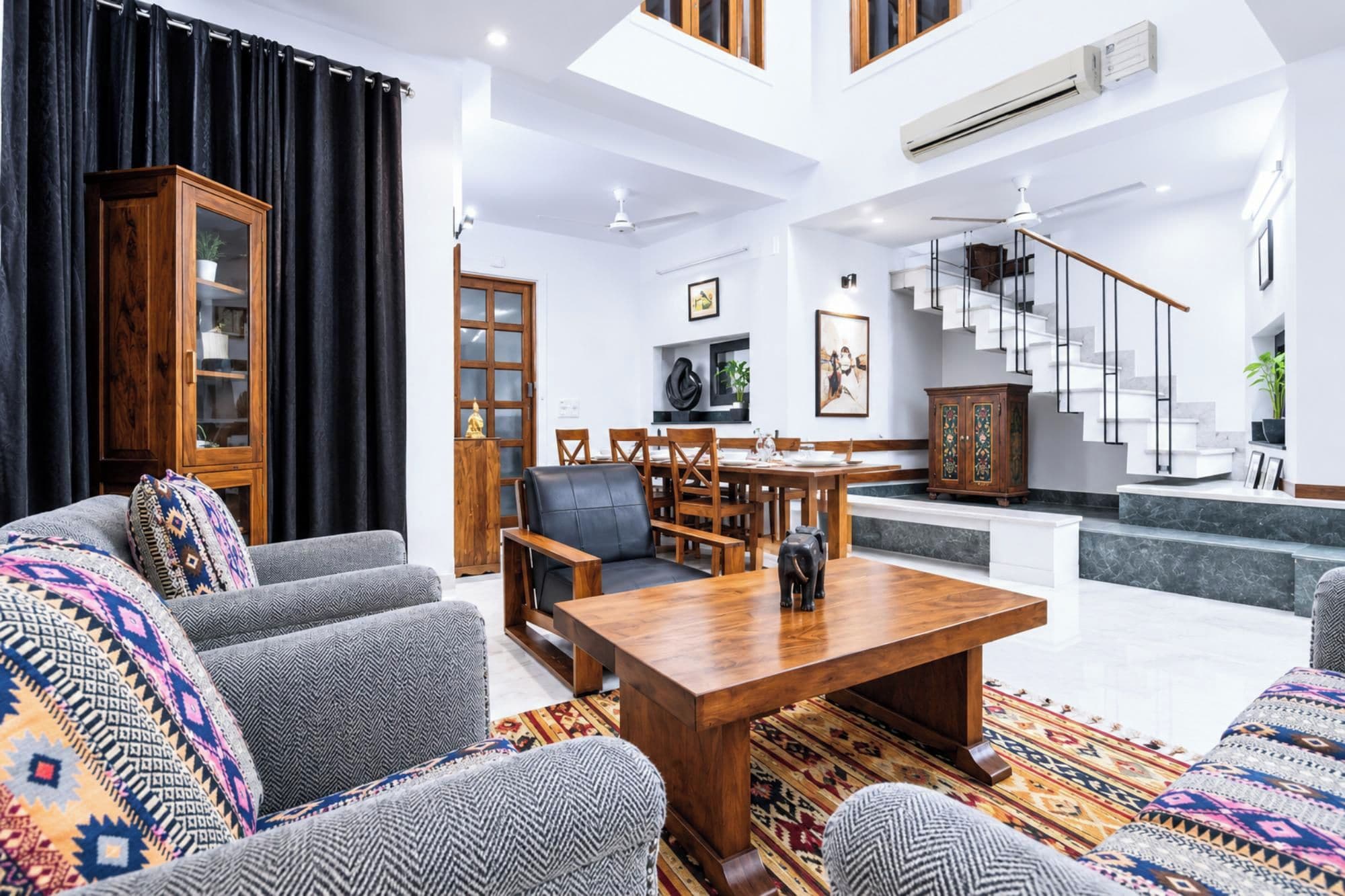 A spacious living area with a high ceiling, a dining table, and a staircase leading to an upper floor.