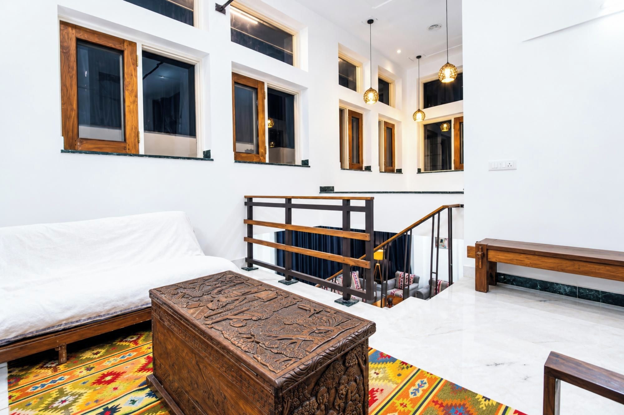A modern interior with a white sofa, a wooden chest, and a staircase with a railing.