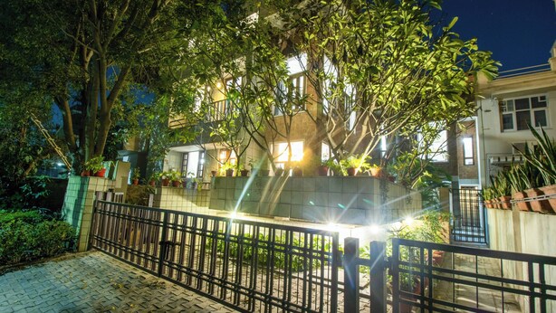 Un área residencial cerrada con un camino pavimentado, árboles y un edificio con ventanas iluminadas por la noche.