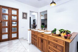A modern kitchen with wooden cabinets, a dining area with a table set for four, and a fruit basket on the counter. - Opulent Antique 6BR Villa in Gurugram (Gurugram)
