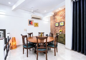 A dining area with a round table, six chairs, and a decorative Buddha statue. - Opulent Antique 6BR Villa in Gurugram (Gurugram)