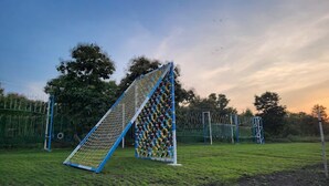 A soccer goal with a net and colorful rings, set in a grassy field with trees and a fence in the background.