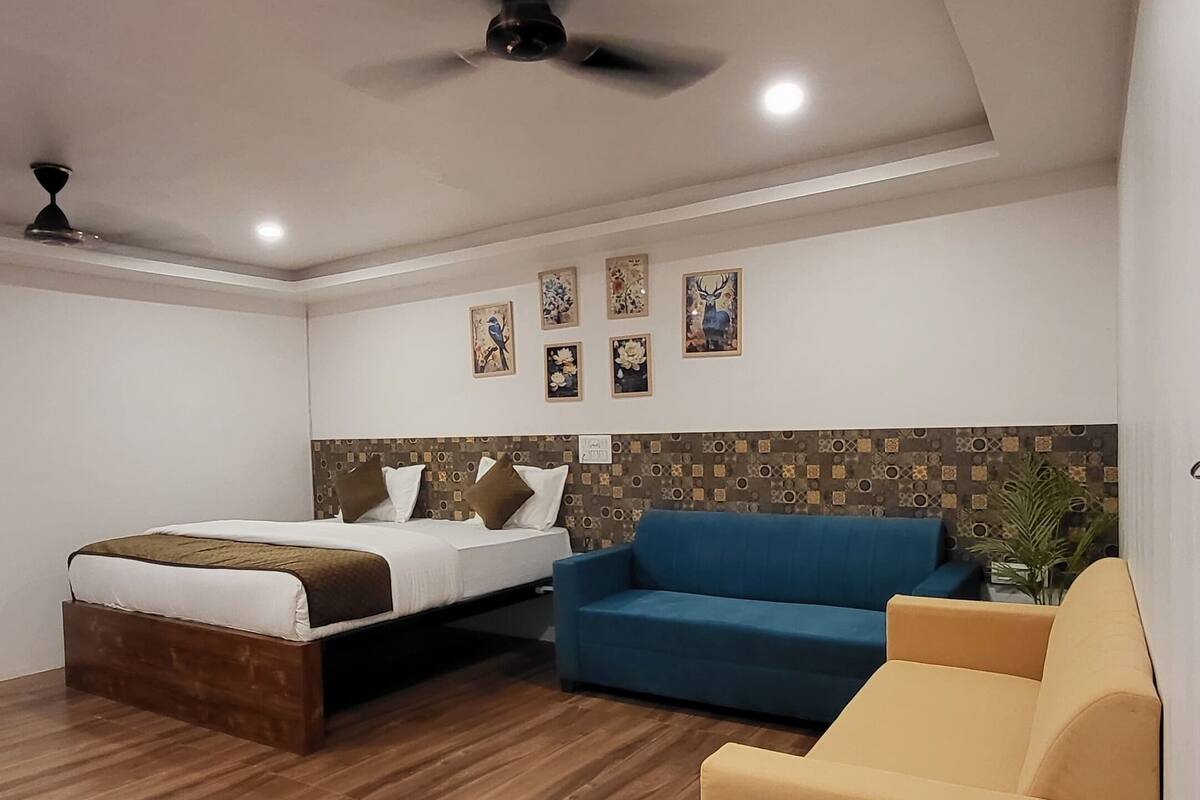 Ein modernes Hotelzimmer mit Holzboden, einem Bett, einem blauen Sofa und einem gelben Sessel.