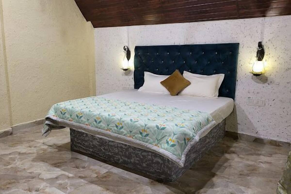 Ein Schlafzimmer mit einem Bett, einem Kopfteil, zwei Wandlampen und einer gemusterten Bettdecke.