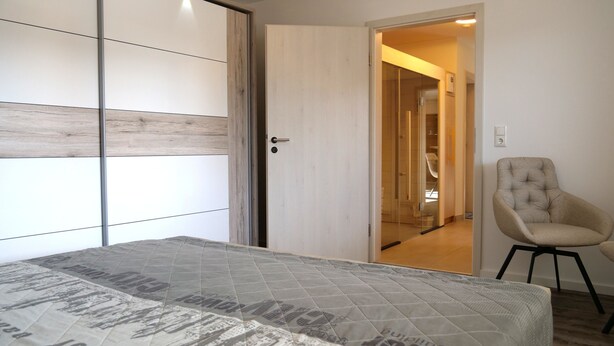 A bedroom with a bed, a chair, and a wardrobe with sliding doors. - Wellness in the Eifel for Ages 16 and Up (Mechernich)