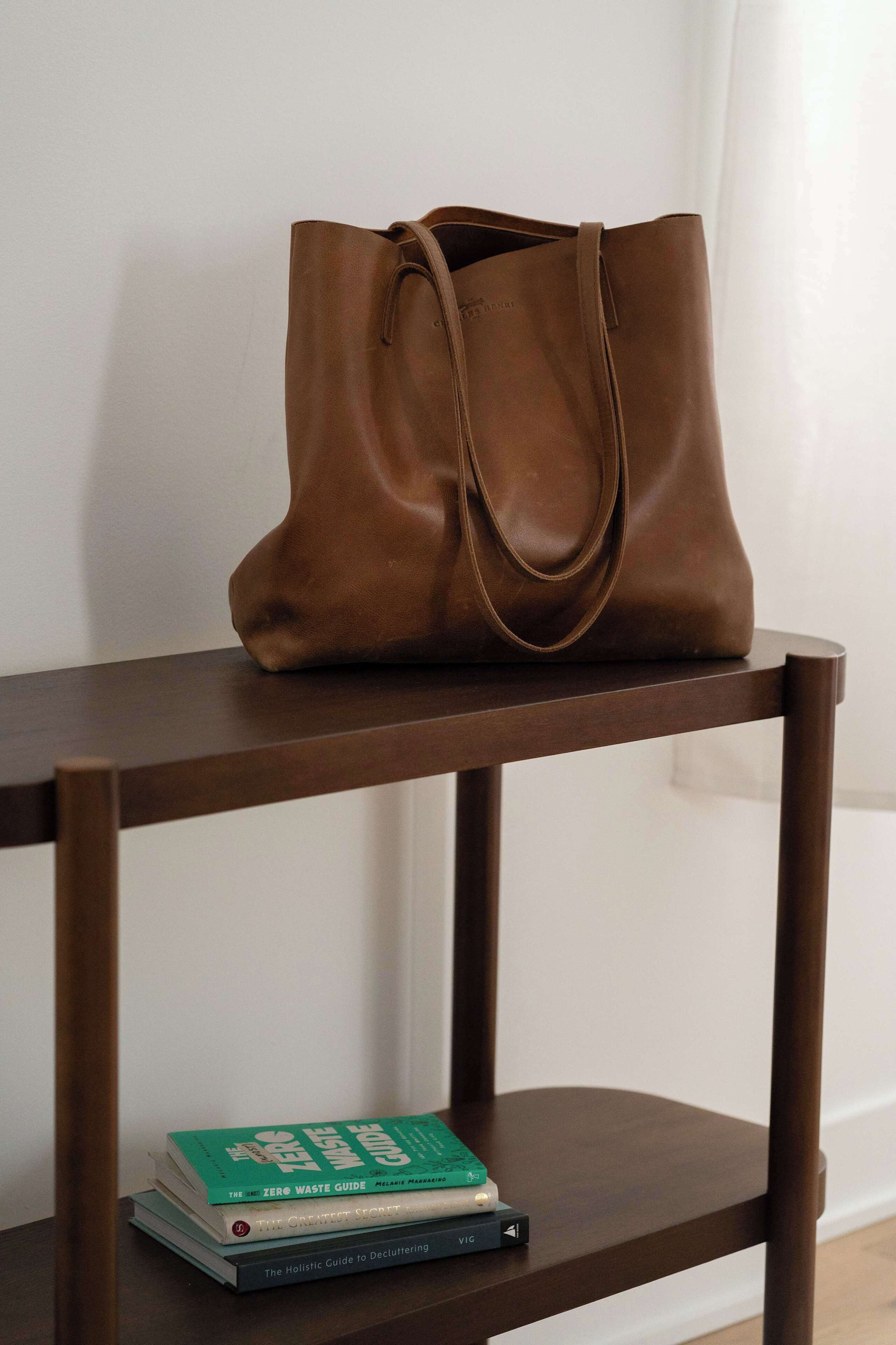 Eine braune Ledertasche auf einem Holzregal, darunter liegen zwei Bücher.