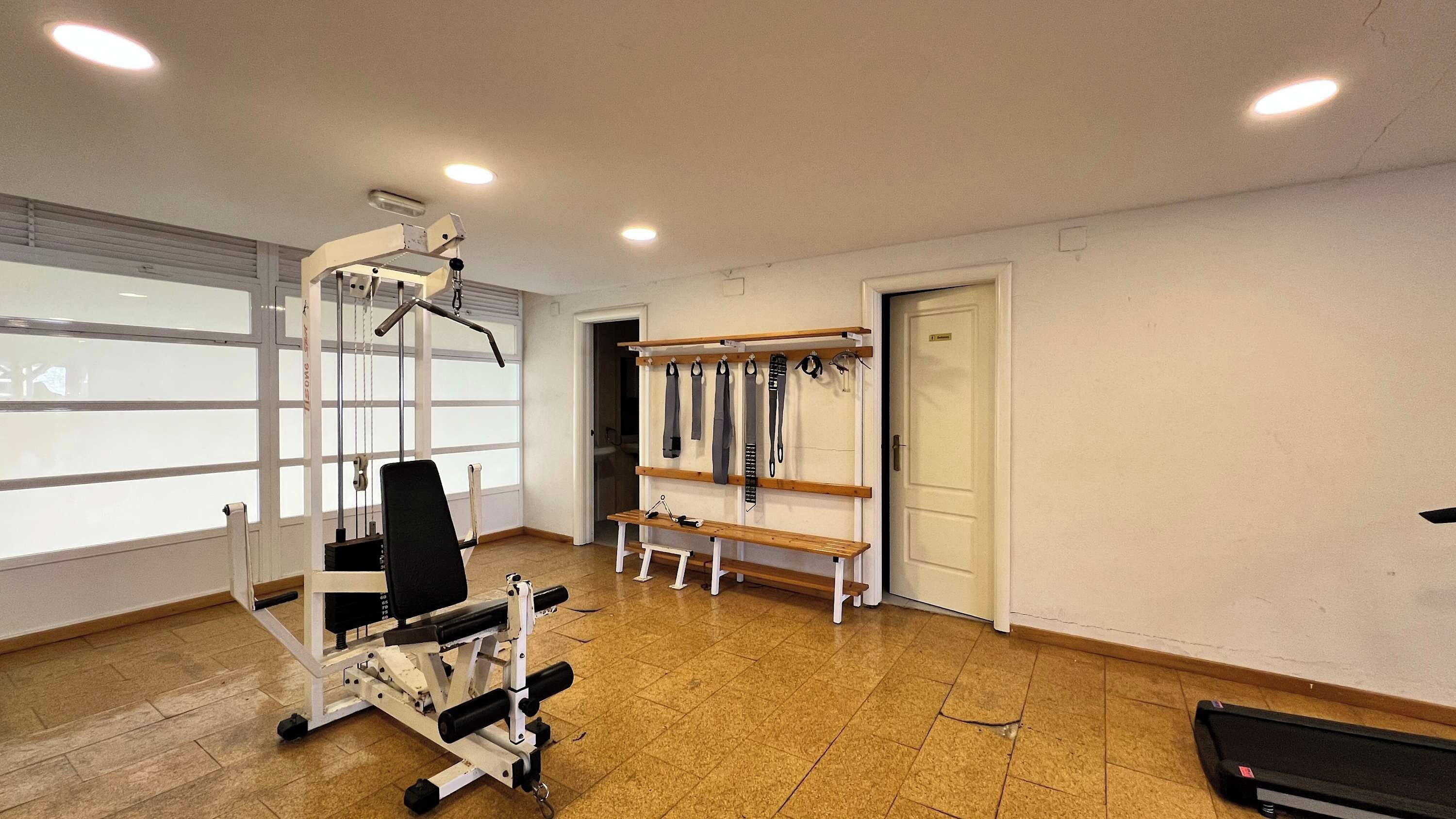 Un gimnasio con equipo de ejercicio, una banca y un estante con correas.