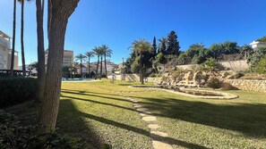A landscaped garden with a pool, palm trees, and a stone wall.