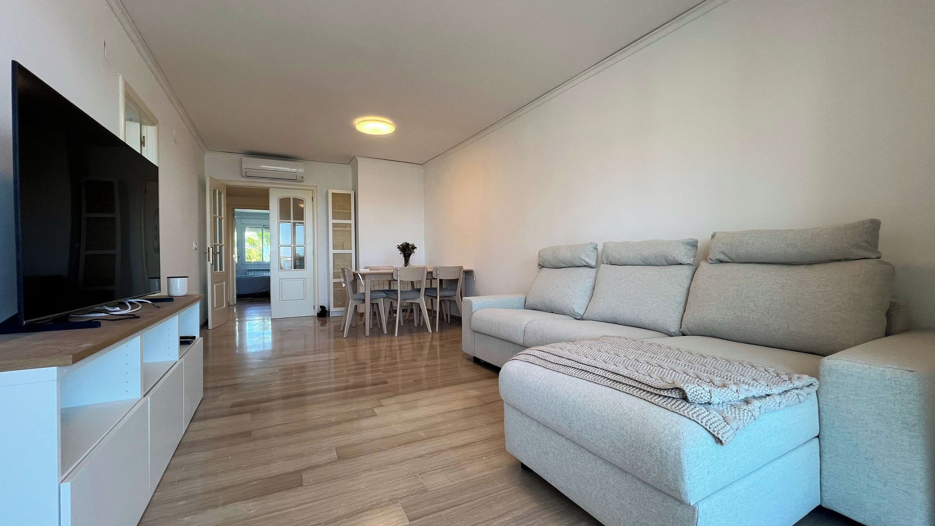 Een moderne woonkamer met een bank, televisie en een eethoek met stoelen en een tafel.