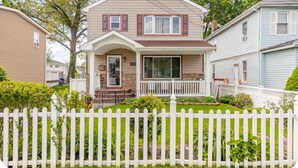 A two-story house with a front porch, a picket fence, and a well-maintained lawn. - Charming Urban3-bedroom  apartment in Hempstead with WiFi and AC (Hempstead)