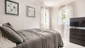 A bedroom with a bed, a dresser, a TV, and two framed artworks on the wall. - Charming Urban3-bedroom  apartment in Hempstead with WiFi and AC (Hempstead)
